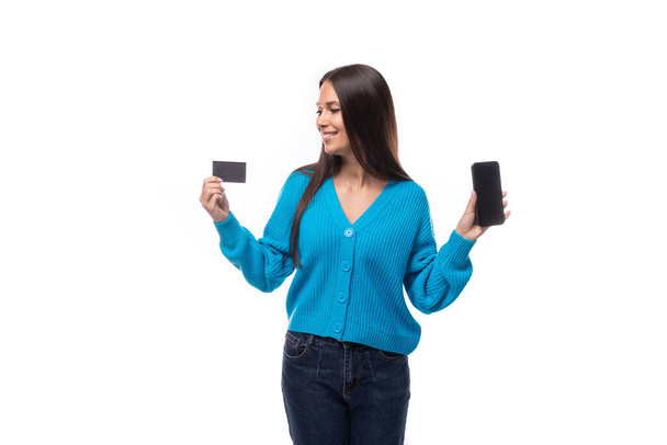 nuori kaunis eurooppalainen brunette nainen pukeutunut sininen villatakki omistaa pankkikortin mockup ja älypuhelin. - Valokuva, kuva