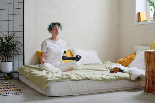 Adolescente con brazo protésico meditando en la cama por la mañana - Foto, imagen
