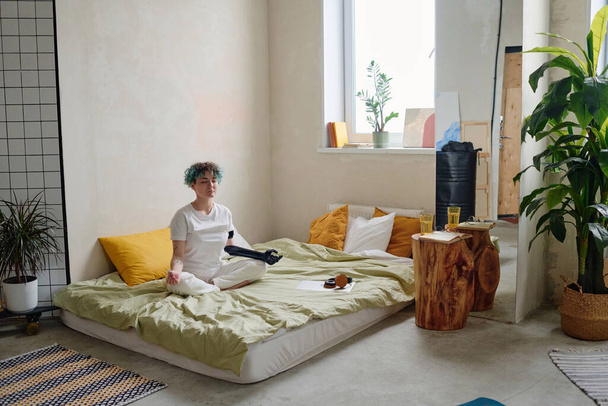 Rauhallinen tyttö vammaisen henkilön kanssa istuu sängyssä ja meditoi - Valokuva, kuva