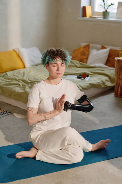 Дівчина з протезною рукою тримає руки в мудрах, коли практикує колінний асан вдома - Фото, зображення
