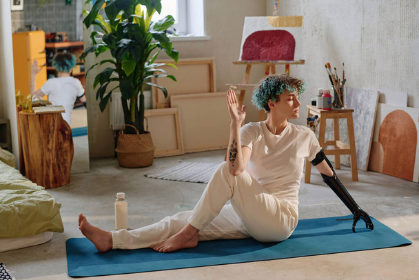 Кучерява дівчина з біонічною рукою робить круту позу на йога килимок - Фото, зображення