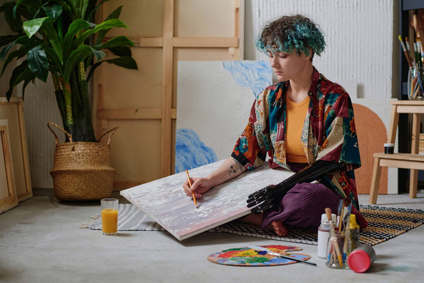 Chica adolescente creativa con el brazo protésico bosquejo dibujo sobre lienzo en el estudio - Foto, imagen