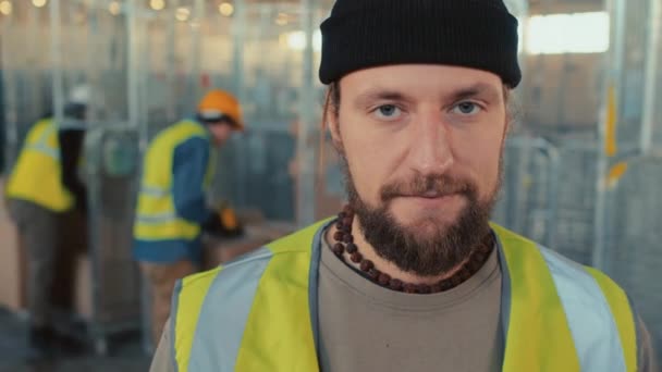 Gros plan ralenti portrait de caucasien barbu entrepôt travailleur en bonnet souriant et regardant caméra à l'intérieur - Séquence, vidéo