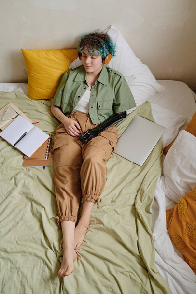 Dziewczyna z protezą ramienia relaks na łóżku i słuchanie muzyki w słuchawkach z zamkniętymi oczami - Zdjęcie, obraz