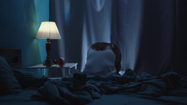 Jonge vermoeide vrouw 's nachts wakker zittend op het bed kijkend naar de wekker en lijdend aan slapeloosheid en nachtmerrie. Kopieerruimte - Video