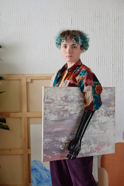 Retrato de una chica seria con un brazo protésico sosteniendo la imagen que dibujó - Foto, imagen