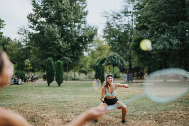 Houkuttelevat urheilijat pelaavat sulkapalloa puistossa. Ystävät pitävät hauskaa ja treenaavat ulkona. Sopii naisille, joilla on upea kehon muoto, nauttia liikunnasta luonnollisessa ympäristössä. - Valokuva, kuva