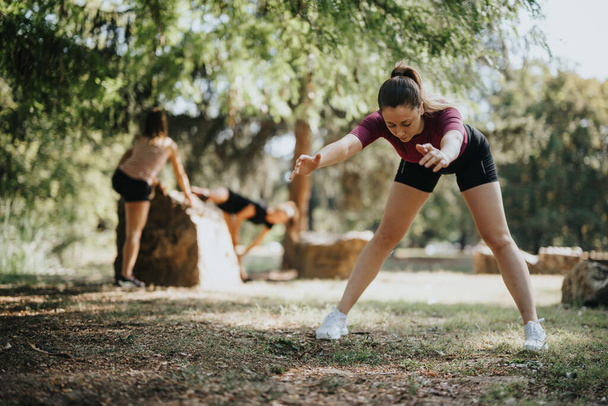 Fit meisjes stretchen en genieten van pre-workout oefeningen in een stadspark. Actief en vrolijk, ze trainen buiten samen, omarmen een gezonde levensstijl. - Foto, afbeelding