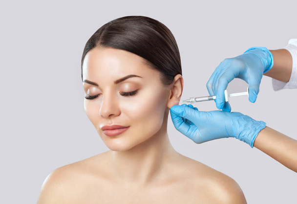El médico cosmetólogo hace el procedimiento de inyecciones para alisar las arrugas y contra la flacidez de la piel en el lóbulo de la oreja de una hermosa, joven mujer en un salón de belleza. - Foto, Imagen