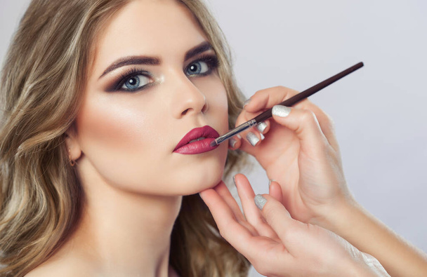 The make-up artist paints the lips of a beautiful woman,  completes the day's make-up in the beauty salon. Professional skin care. - Valokuva, kuva