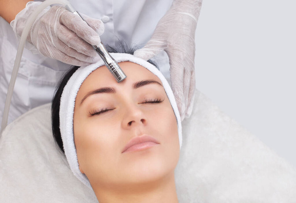 Kosmetolog wykonuje zabieg Mikrodermabrazja skóry twarzy pięknej, młodej kobiety w salonie kosmetycznym.Kosmetologia i profesjonalna pielęgnacja skóry. - Zdjęcie, obraz
