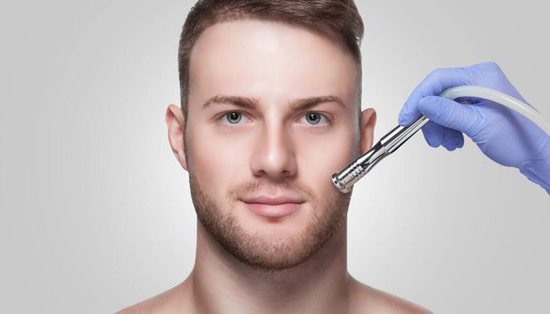 A cosmetologist is making the procedure Microdermabrasion of the facial skin in a beauty salon. Cosmetology for men and professional skin care. - Photo, Image