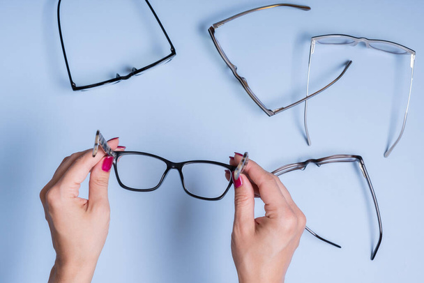 Szemüveg női kézben, kék háttérrel. Optikai áruház, látás teszt, stílusos szemüveg koncepció. - Fotó, kép