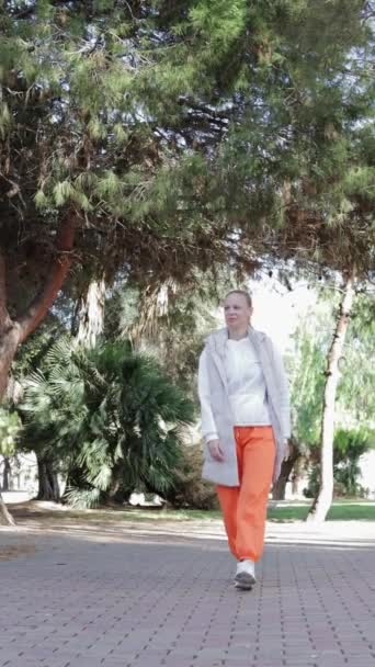 a happy girl of European appearance in a tracksuit walks through a beautiful park, vertical video. High quality footage - Footage, Video