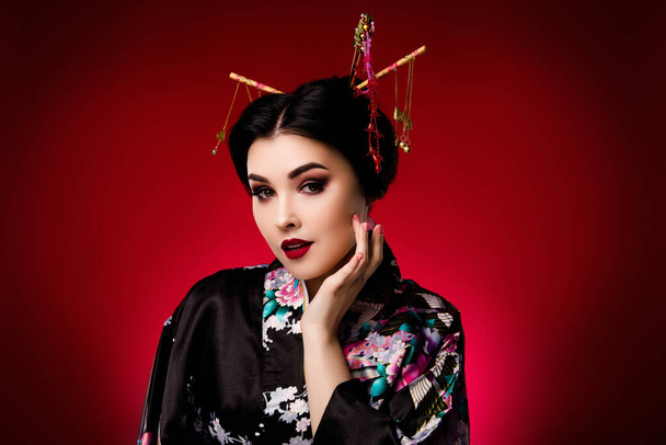 Foto de elegante señora vestida kimono negro ropa coreana mano tacto cara aislada en rojo degradado color fondo. - Foto, imagen