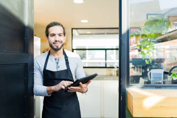 Portrait d'un homme hispanique attrayant et propriétaire d'entreprise ouvrant son propre restaurant ou café à la recherche heureux - Photo, image