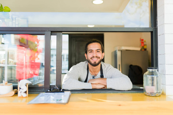 Kahve dükkanında kahve sipariş ederken gülümseyen yakışıklı Latin erkek barmen. - Fotoğraf, Görsel