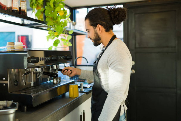 Mexikanischer Mann mit Schürze, der als Barista im Café arbeitet und mit der Espressomaschine ein Getränk zubereitet - Foto, Bild