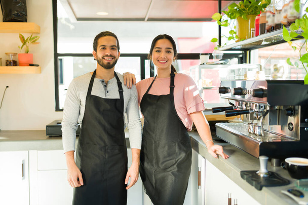 Önlüklü mutlu bir genç adam ve kadın kahve dükkanında neşeli baristalar gibi çalışıyor ve gülümsüyor. - Fotoğraf, Görsel