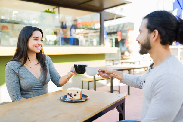Boldog vonzó pár a 20-as éveikben mosolygós, amelynek egy romantikus dátum a szabadtéri kávézóban, és kávézás desszerttel - Fotó, kép
