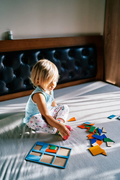 Klein meisje zittend op het bed voor de puzzelstukjes. Hoge kwaliteit foto - Foto, afbeelding
