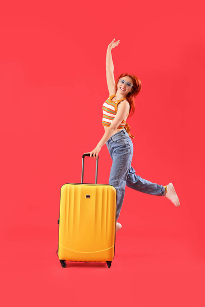 Jumping female tourist with suitcase on red background - Photo, Image