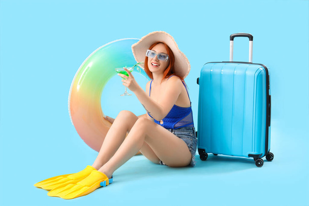 Touriste féminine avec valise, cocktail et anneau de natation sur fond bleu - Photo, image