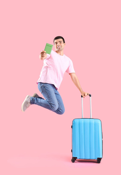 ピンクの背景にスーツケースとパスポートで男性の観光客をジャンプ - 写真・画像