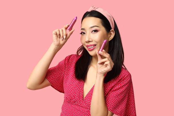 Bella donna asiatica con diversi rossetti su sfondo rosa - Foto, immagini