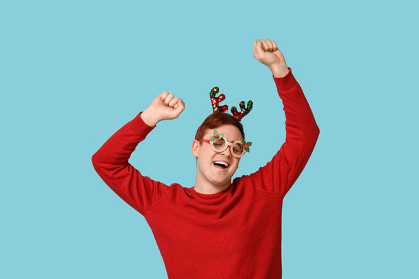 Веселий молодий чоловік у теплому светрі, оленячий пояс і новітні окуляри на синьому фоні - Фото, зображення