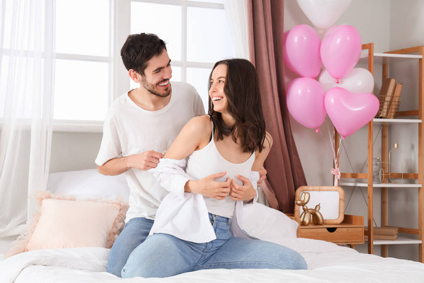 Счастливая молодая пара, сидящая в спальне в День Святого Валентина - Фото, изображение