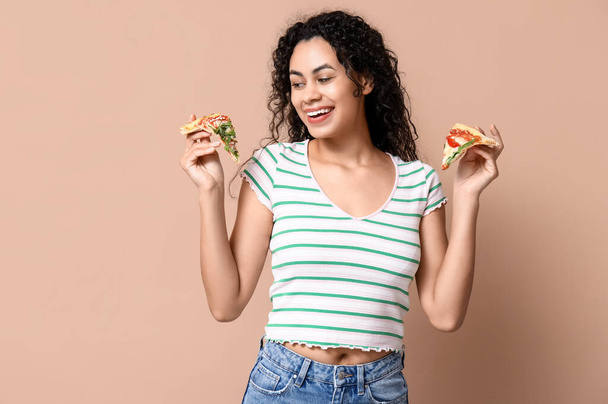 Schöne junge glückliche afroamerikanische Frau mit Scheiben leckerer Pizza auf beigem Hintergrund - Foto, Bild