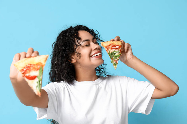 Güzel, genç, mutlu, Afro-Amerikan kadın mavi arka planda lezzetli pizzalar dilimliyor. - Fotoğraf, Görsel