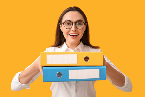 Молода бізнес-леді з папками документів на жовтому тлі - Фото, зображення