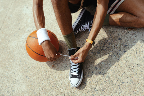 Спортсмен завязывает шнурки на кроссовках перед игрой в стритбол - Фото, изображение