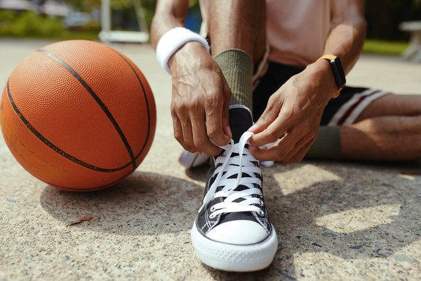 Καλλιεργημένη εικόνα του παίκτη streetball δένοντας κορδόνια παπουτσιών πριν από το παιχνίδι - Φωτογραφία, εικόνα