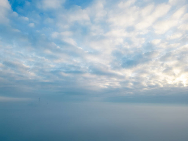 Tento obraz, zachycený trubcem nad mlhou, zobrazuje klidnou oblohu, kde se měkká bílá barva altokumulovaných mraků setkává s mírným svahem svítání. Pokrývka mlhy vytváří - Fotografie, Obrázek