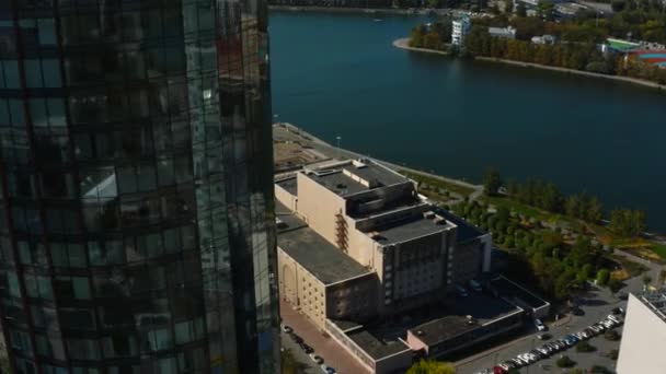 Top view of glass facade of high-rise building with landscape of city and river. Stock footage. Beautiful landscape of modern city with glass buildings. Glass skyscrapers with green landscapes of - Footage, Video
