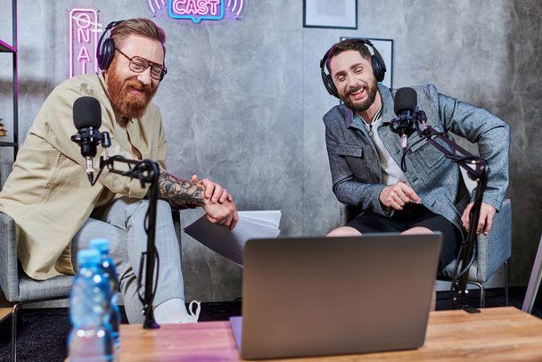 hombres elegantes de buen aspecto con barbas y auriculares discutir preguntas en el estudio durante el podcast - Foto, Imagen