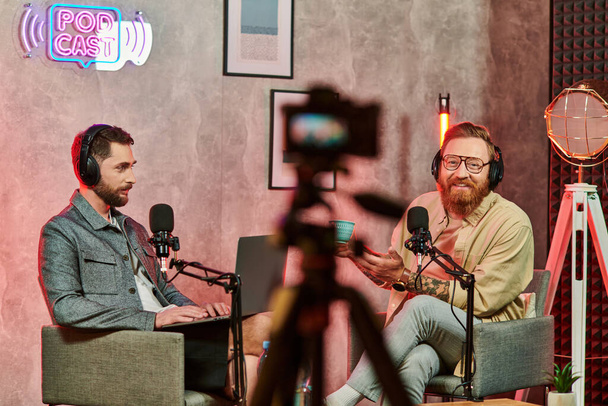 hommes gais dans des vêtements confortables avec café et ordinateur portable lors de leur discussion sur podcast - Photo, image