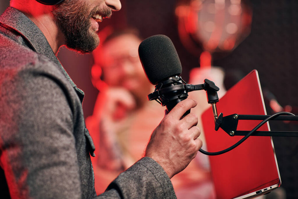 corte visão focada do homem barbudo com microfone com seu entrevistador desfocado no podcast - Foto, Imagem