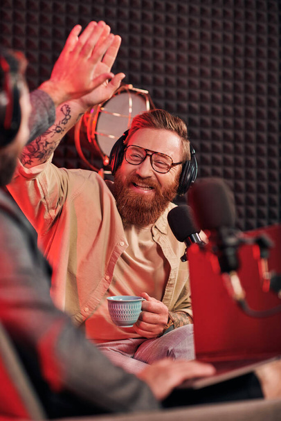 μουσάτος συνεντευξιαστής με γυαλιά να κάνει κόλλα πέντε με τον θολή καλεσμένο του κατά τη διάρκεια του podcast - Φωτογραφία, εικόνα
