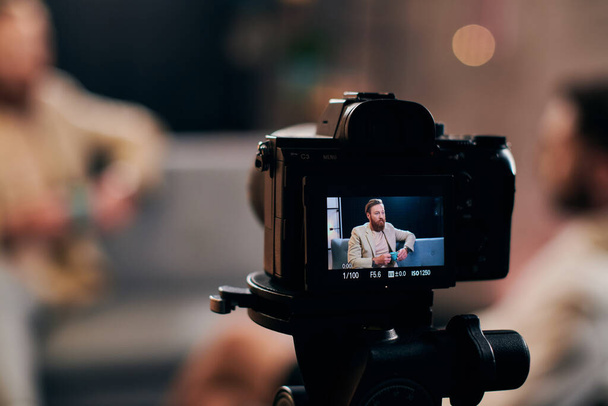 εστίαση στην κάμερα γυρίσματα κομψό θολή άνθρωπος με γενειάδα σε κομψή ενδυμασία συζητώντας ερωτήσεις - Φωτογραφία, εικόνα