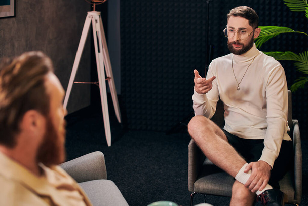 スタジオのインタビュアーの隣に座ってエレガントな服を着た魅力的なひげ付き男 - 写真・画像