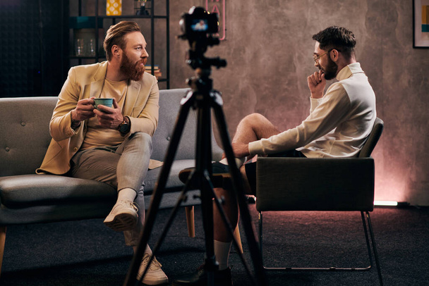 omistautuneet miehet, joilla on parrat tyylikkäissä puvuissa istuvat ja keskustelevat kysymyksistä haastattelun aikana - Valokuva, kuva