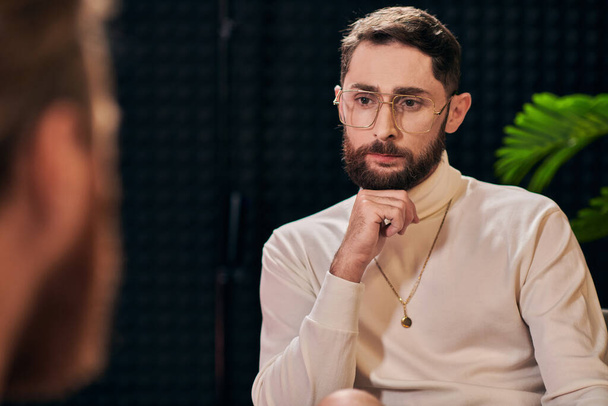 handsome bearded man with glasses in elegant outfit sitting and looking at his interviewer - Photo, Image