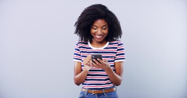 Чорна жінка, друкуючи на смартфоні і посміхаючись в студії, ізольована на білому фоні макет простору. Портрет, телефон або щаслива африканська людина прокручується на мобільному додатку, електронній пошті або пошуку в Інтернеті в соціальних мережах. - Кадри, відео