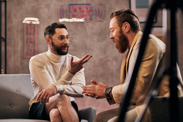 エレガントなスタイリッシュな服装の2人のハンサムなひげ付き男性が座ってインタビューの質問を議論 - 写真・画像