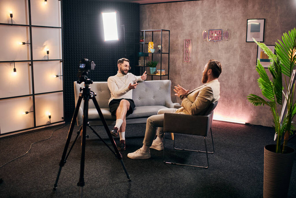 gut gelaunte, stylische Männer mit schickem Stil sitzen im Studio und diskutieren Interviewfragen - Foto, Bild