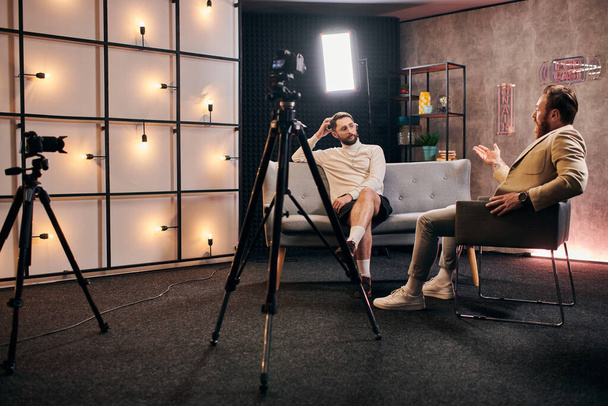 dwóch eleganckich mężczyzn z brodami z eleganckim stylu siedzi i omawia pytania wywiadu w studio - Zdjęcie, obraz